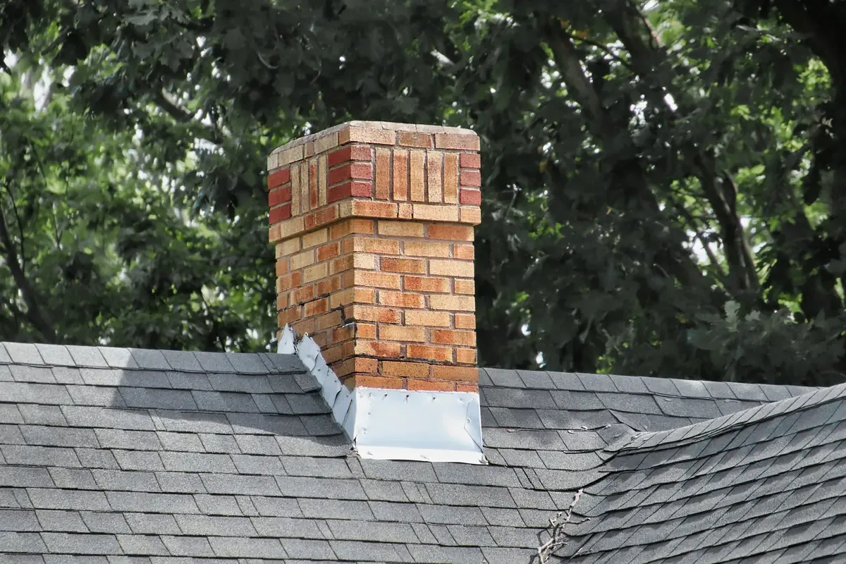 Brick chimney with metal flashing where it meets a gray asphalt shingle roof