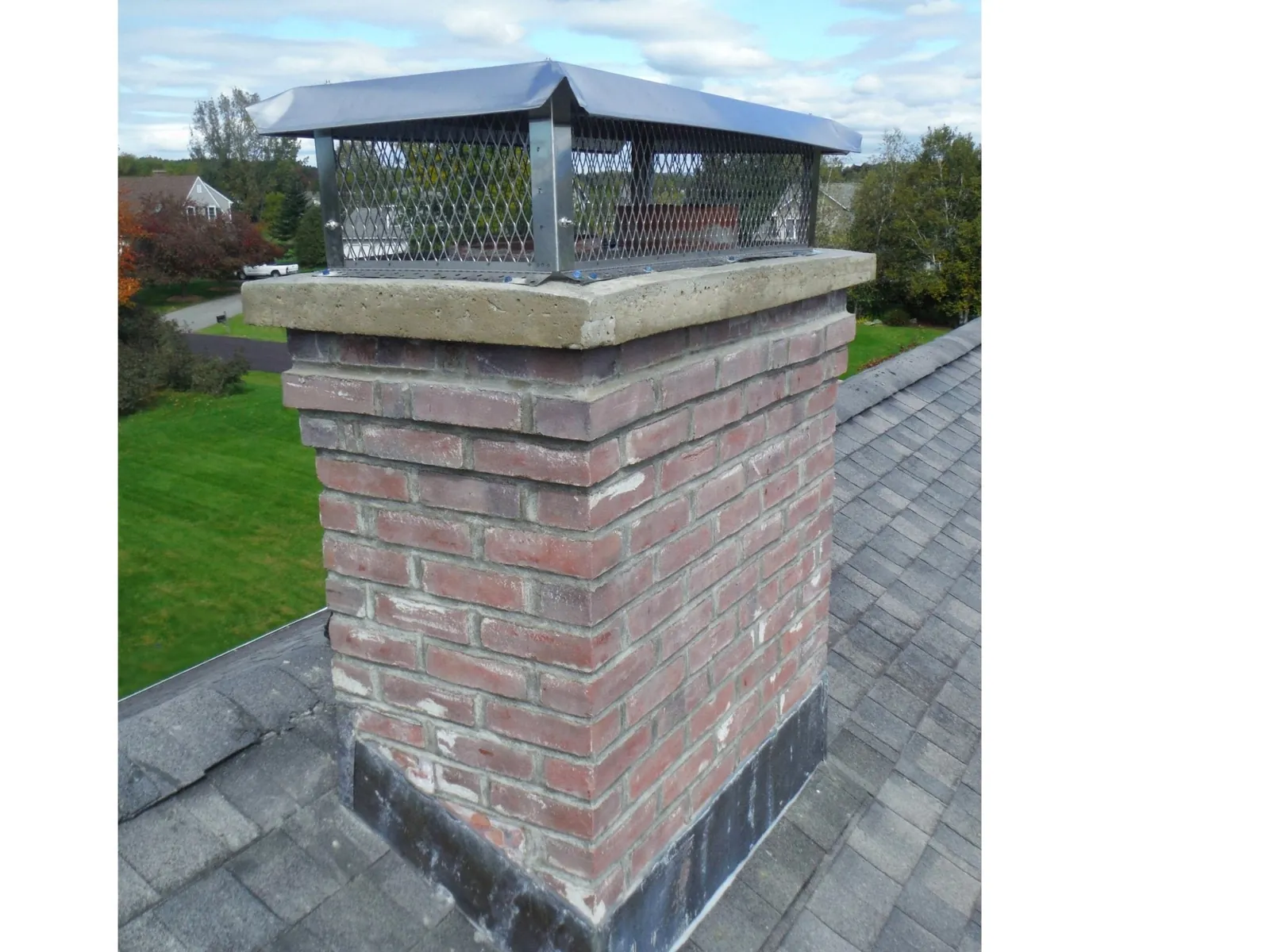 Stainless steel chimney cap with mesh sides on a brick chimney with a concrete crown
